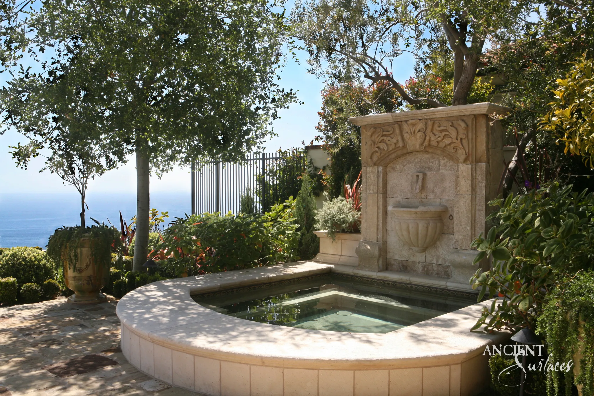 Carved limestone wall fountain beside a garden spa pool overlooking the ocean
